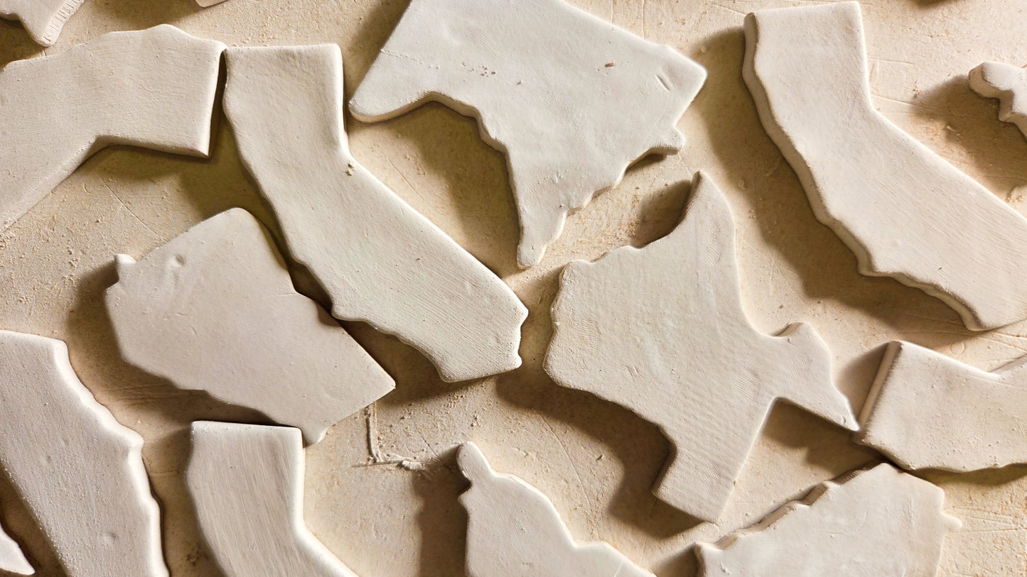 Raw ceramic state shape magnet blanks including Texas, Minnesota, Louisiana, and Georgia before glazing and personalization into custom souvenir magnets
