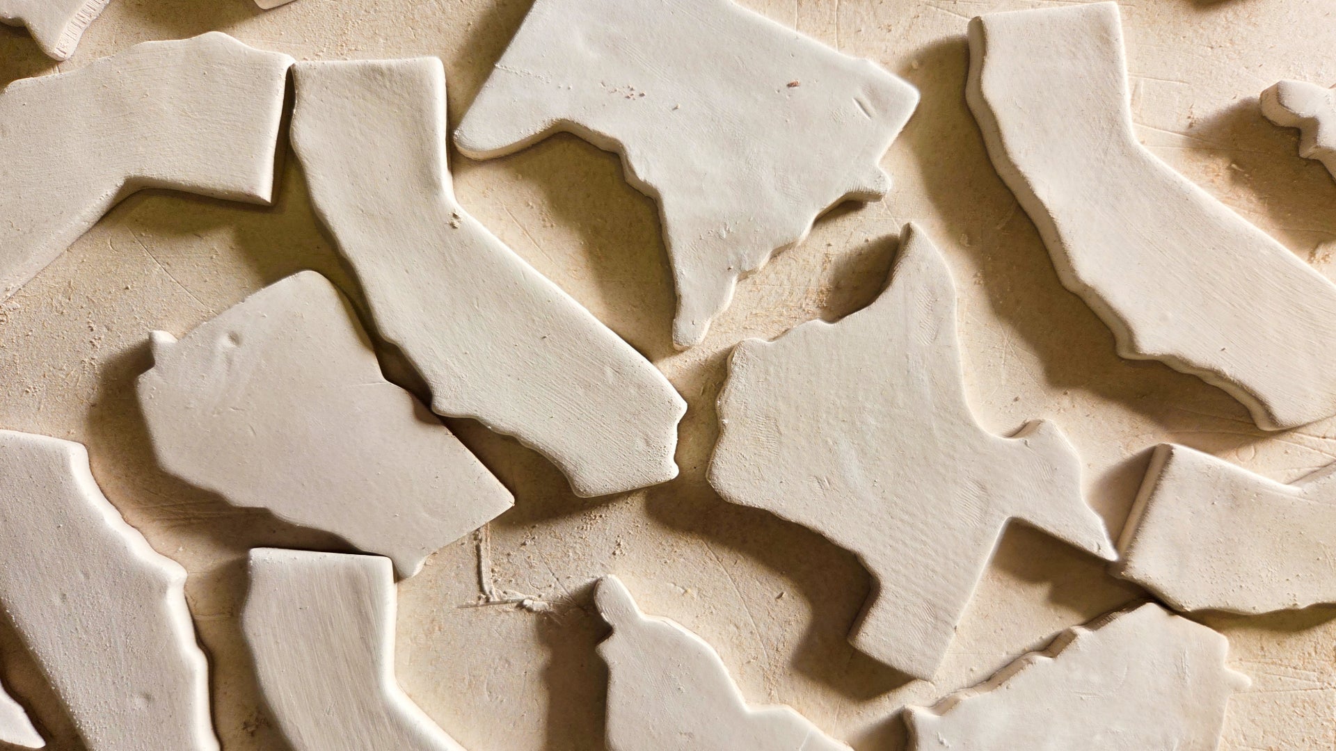 Raw ceramic state shape magnet blanks including Texas, Minnesota, Louisiana, and Georgia before glazing and personalization into custom souvenir magnets